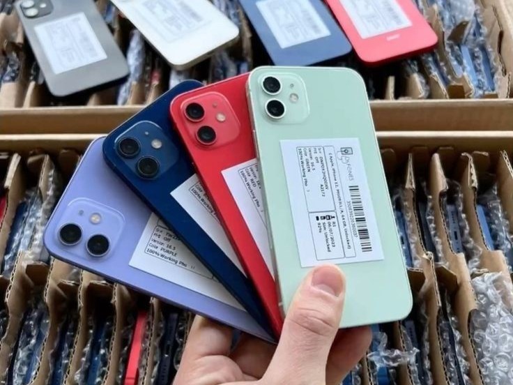 iPhones 12 em várias cores segurados na mão sobre caixas de atacado