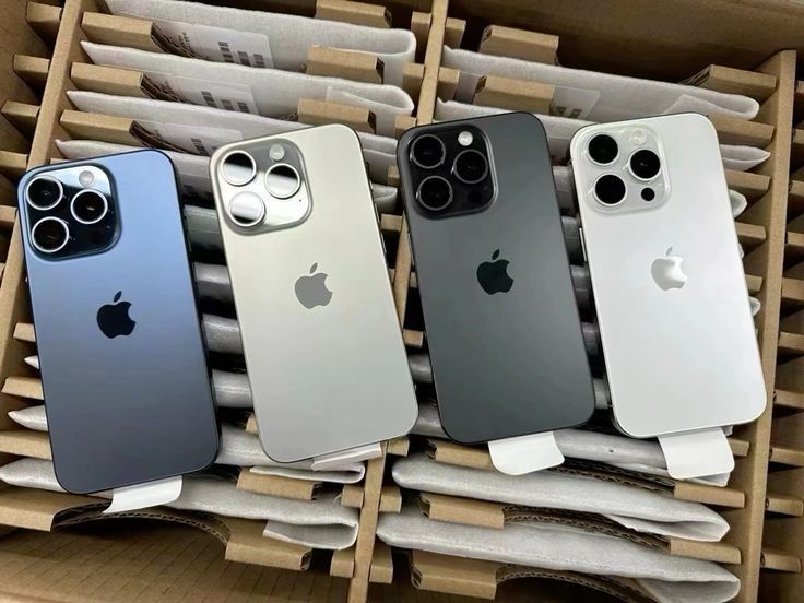 iPhones 15 Pro Max em titânio azul, natural, preto e branco dentro de uma caixa de atacado